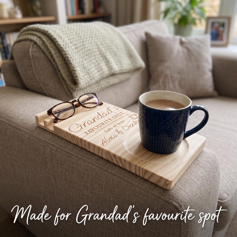 May include: A rectangular light-colored wooden sofa arm tray featuring a circular coaster indentation and a slot for glasses. The wood is engraved with the text "Grandad's FAVOURITE SPOT" and "lots of love Alma & Dexter" with a coffee cup icon.