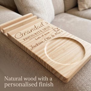 May include: A light-colored wooden sofa arm tray featuring a circular coaster indentation and a slotted stand. The surface is engraved with the text Grandad's FAVOURITE SPOT, Lots of love, and Jackson, Otto & Mia x, along with a small coffee cup icon.