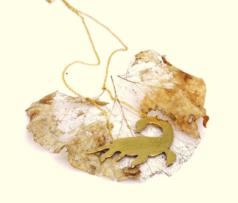 May include: A gold chain necklace with a gold scorpion pendant. The pendant is a silhouette of a scorpion and is resting on a dried leaf.