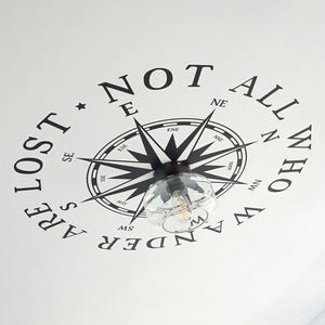 May include: A white ceiling with a black compass rose design and the words "NOT ALL WHO WANDER ARE LOST" in a circular arrangement. A clear glass light fixture hangs below the compass.
