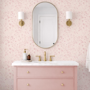 Könnte beinhalten: Ein rosa Badezimmerwaschtisch mit goldenen Armaturen und einer weißen Arbeitsplatte. Der Waschtisch hat zwei Schubladen und ein unteres Regal. Eine florale Tapete und ein schwarz-weiß gefliester Boden vervollständigen das Badezimmerdesign. Ein Spiegel und Wandleuchten sind an der Wand montiert.