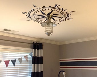 May include: A nautical themed nursery with a compass ceiling decal, a striped curtain, and a crib with a "dream big" pillow.