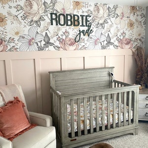 May include: A nursery room with a crib, a rocking chair, and a dresser. The walls are covered in floral wallpaper with the names "Robbie" and "Jade" written on the wall.