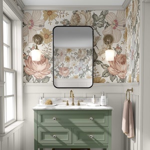 May include: A green bathroom vanity with a white marble countertop and a black framed mirror. The vanity has three drawers and a lower shelf. The walls are covered in floral wallpaper with a white background.