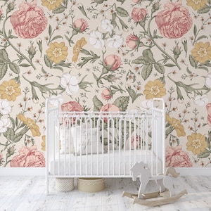 Op de afbeelding: Een wit babybedje met een bloemenbehang met roze, gele en witte bloemen. Het babybedje heeft een wit matras en een wit kussen met de tekst "Goedenacht" erop.
