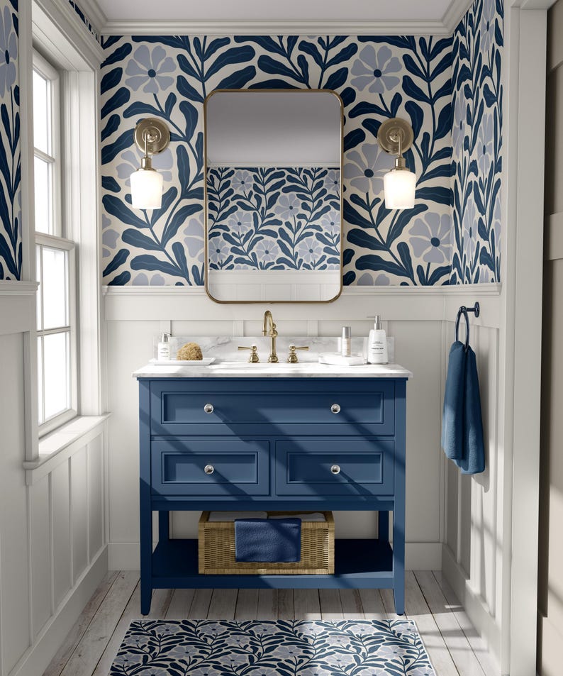May include: A blue bathroom vanity with a white countertop and a gold faucet. The vanity has three drawers and a lower shelf. The bathroom has white walls with blue floral wallpaper and a gold framed mirror. There is a blue towel hanging on a towel rack.