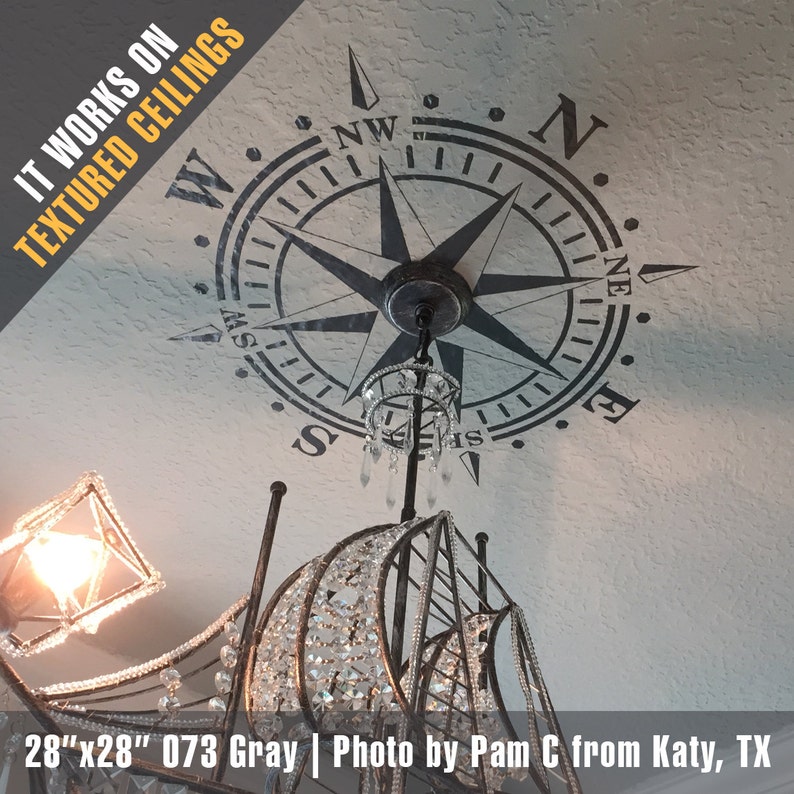 May include: A black and white compass design wall decal with the words "IT WORKS ON TEXTURED CEILINGS" in the top left corner. The decal is 28 inches by 28 inches and is shown on a textured ceiling with a chandelier.