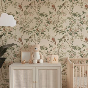 May include: A nursery room with beige wallpaper featuring a repeating pattern of birds and flowers. A white cloud-shaped lamp is mounted on the wall. A white teddy bear sits on a white dresser with a wooden frame and a wicker front. A wooden crib with a white mattress and a white and brown patterned sheet is in the background. The dresser has a wooden block with the letters 'A' and 'C' on it.