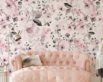 May include: A tufted light pink sofa with a fuzzy rectangular pillow sits against a wall covered in floral wallpaper featuring large watercolor-style pink and grey flowers, leaves, and stems on a light cream background with a gold floor lamp.
