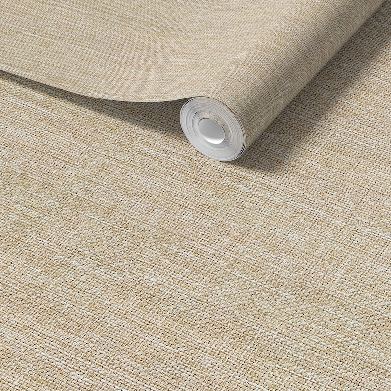 May include: A roll of beige wallpaper with a woven texture. The wallpaper is a neutral color, with a subtle pattern that resembles linen or burlap. The roll is partially unrolled, revealing the paper's thickness and texture.