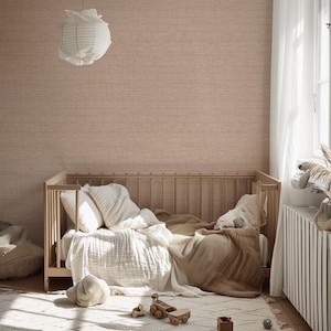 Può includere: Una culla in legno chiaro con biancheria da letto bianca e una coperta marrone. Una lanterna di carta bianca è appesa al soffitto. La stanza ha una palette di colori neutri con un tappeto fantasia e giocattoli di legno.