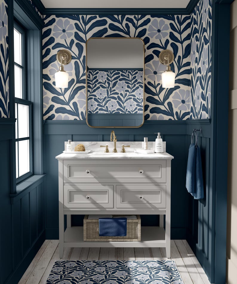 May include: A bathroom with a gray vanity, a gold-framed mirror, and floral wallpaper in navy and light blue. The vanity has a marble countertop, a woven basket, and a navy blue towel. The walls are painted navy blue.