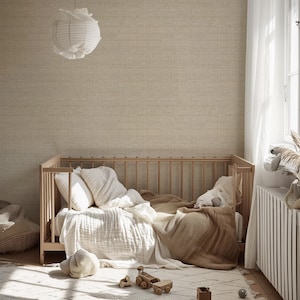 May include: A light wood crib with white bedding, pillows, and a tan blanket. A white paper lantern hangs from the ceiling. A patterned rug and wooden toys are on the floor. The room has a neutral color palette.