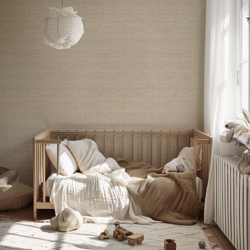 May include: A light wood crib with white bedding, pillows, and a tan blanket. A white paper lantern hangs from the ceiling. A patterned rug and wooden toys are on the floor. The room has a neutral color palette.