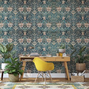 May include: A teal and beige floral wallpaper covers the wall behind a wooden desk and a yellow chair. Potted plants and a woven rug add to the room's decor. A desk lamp and small clock are on the desk.