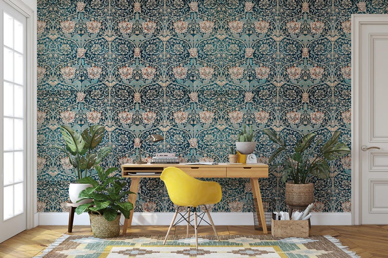 May include: A teal and beige floral wallpaper covers the wall behind a wooden desk and a yellow chair. Potted plants and a woven rug add to the room's decor. A desk lamp and small clock are on the desk.