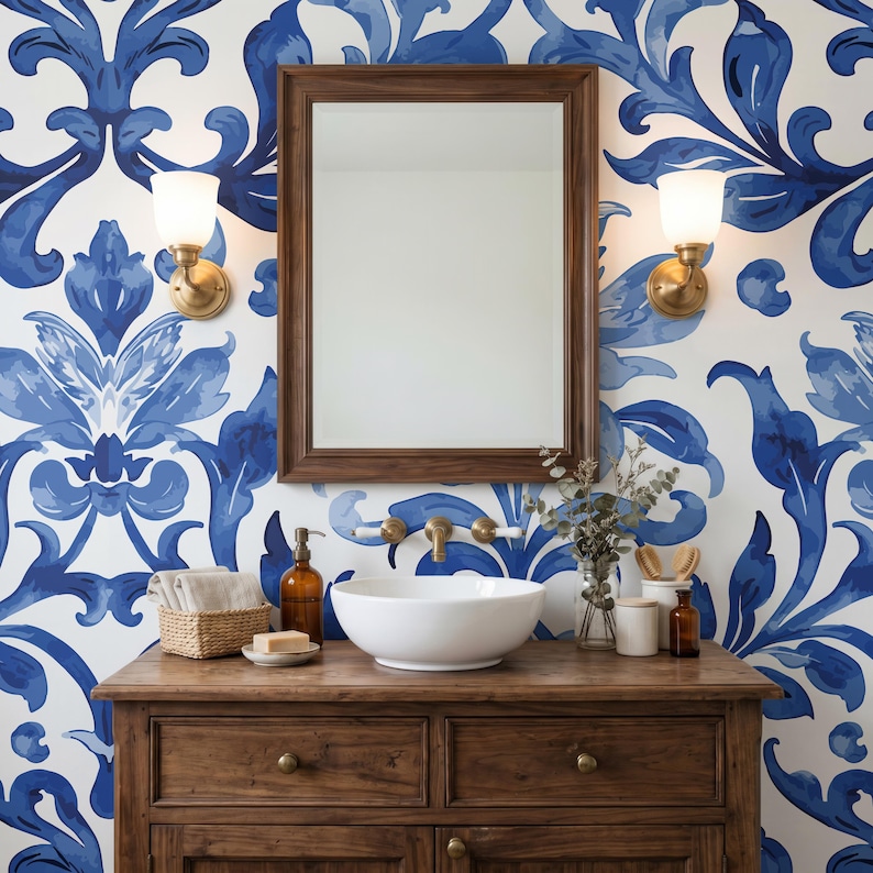 May include: A bathroom vanity featuring a white vessel sink, a wooden cabinet with drawers, and a rectangular mirror. The wall is covered in blue and white damask wallpaper, flanked by two brass wall sconces with white glass shades.