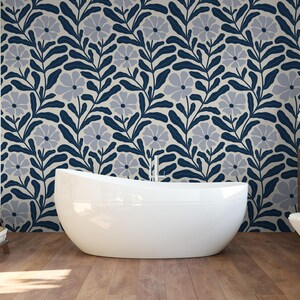 May include: A modern bathroom with a white, oval-shaped bathtub. The wall behind the tub features a floral pattern in navy blue and gray. The floor is made of wood. A wooden shelf with towels and toiletries is on the left.