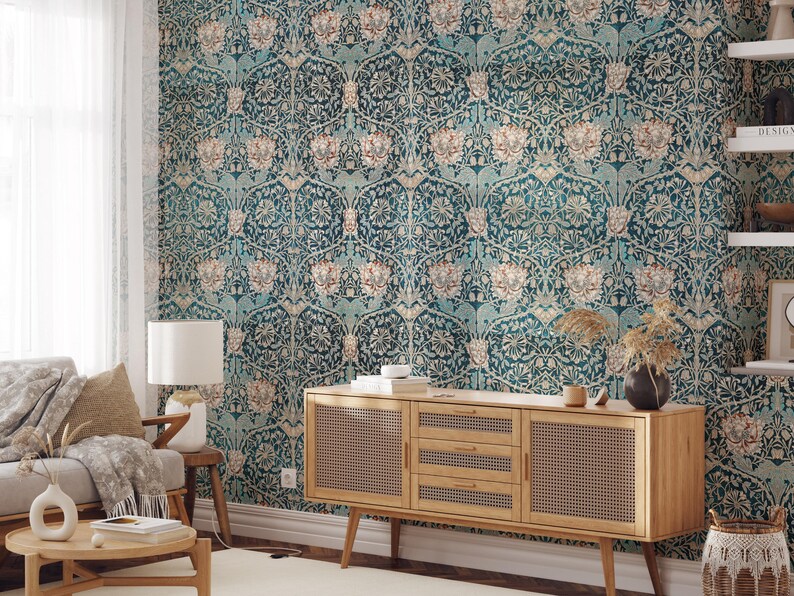 May include: A living room with teal floral wallpaper. A wooden cabinet with woven cane doors sits below the wallpaper. A sofa, side table, and coffee table are in front of the cabinet. A white lamp and a vase with dried plants are on the tables.