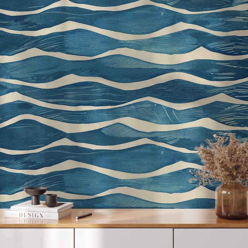 May include: A blue and cream-colored wallpaper with a wave pattern. The design features horizontal, undulating lines in varying shades of blue, with cream-colored wave crests. The wallpaper is displayed on a wooden surface with decorative items.