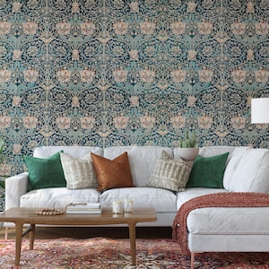 May include: A living room scene featuring a white sectional sofa with green and brown throw pillows, a wooden coffee table, and a patterned rug. The wall is covered in a teal and beige floral wallpaper. Potted plants and a lamp complete the decor.