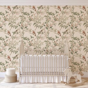 May include: A white cot with a white frilled skirt and a white rocking horse in front of it. The wall behind the cot is covered in a beige wallpaper with a repeating pattern of brown birds and green leaves.
