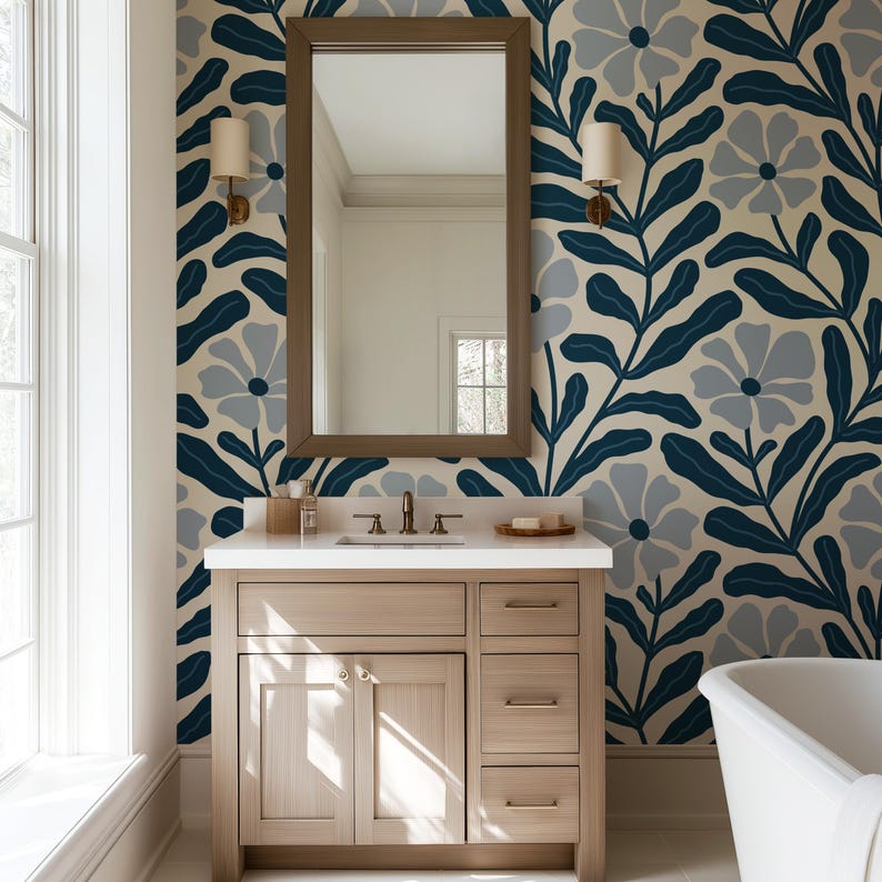 May include: A bathroom with a light wood vanity, a large mirror, and a floral wallpaper pattern in navy blue, gray, and cream. The room includes a white bathtub and sconces.