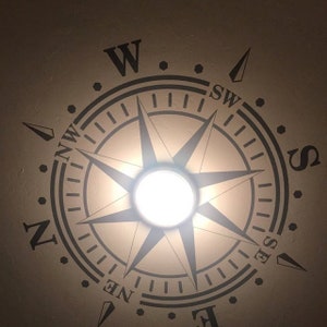 May include: A black and white compass design on a beige ceiling with a white light fixture in the center.