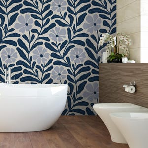 May include: A modern bathroom with a white bathtub and toilet. The wall features a floral pattern in navy blue and gray against a cream background. The floor is made of wooden planks, and there is a decorative shelf with plants.