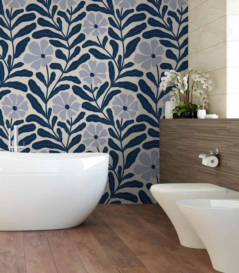May include: A modern bathroom with a white bathtub and toilet. The wall features a floral pattern in navy blue and gray against a cream background. The floor is made of wooden planks, and there is a decorative shelf with plants.