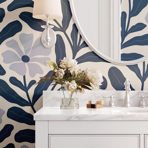 May include: A bathroom scene featuring a white vanity with a marble countertop, a round mirror, and a floral wallpaper in shades of blue and cream. A bouquet of white flowers sits in a clear vase.
