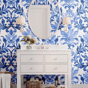 May include: A white bathroom vanity with four drawers and an open bottom shelf, featuring a marble countertop, a silver faucet, and a large oval mirror. The wall is covered in blue and white damask wallpaper with two wall-mounted light fixtures.