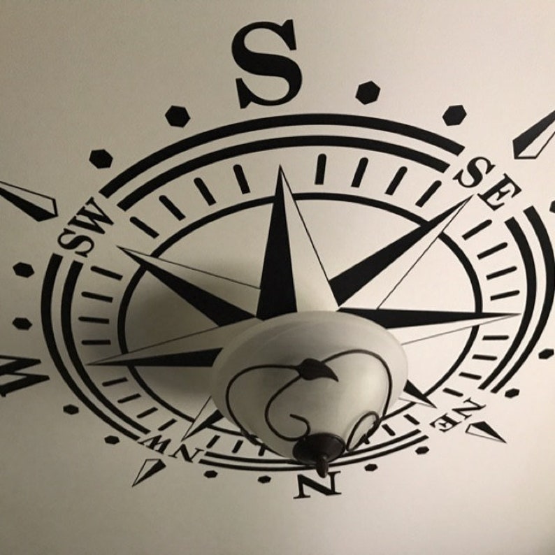 May include: Black and white compass design on a white ceiling. The compass has the cardinal directions N, S, E, and W, as well as the intermediate directions NE, NW, SE, and SW. The compass is centered on a light fixture.