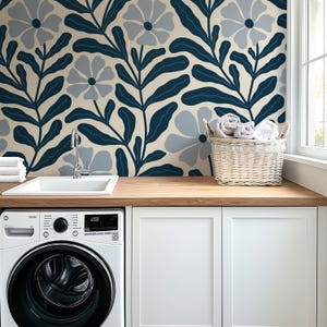 May include: A laundry room with a white washing machine, sink, and cabinets. A wooden countertop and a floral wallpaper with navy blue and light blue flowers and leaves. A wicker basket holds rolled towels.