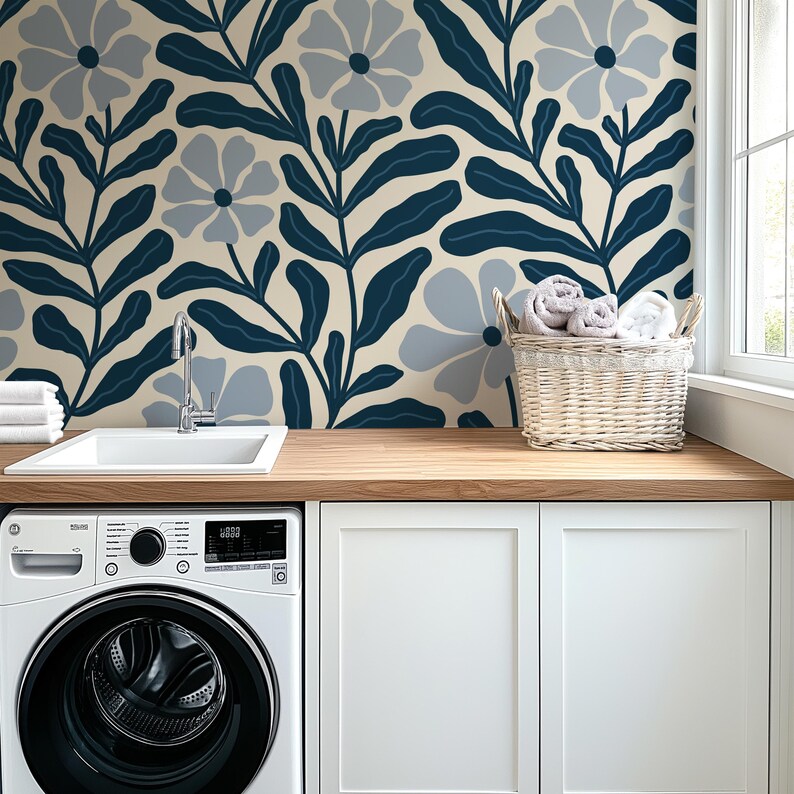 May include: A laundry room with a white washing machine, sink, and cabinets. A wooden countertop and a floral wallpaper with navy blue and light blue flowers and leaves. A wicker basket holds rolled towels.