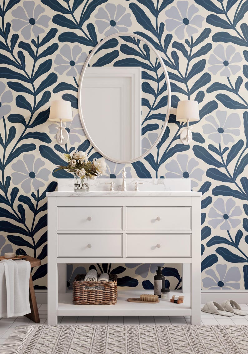 May include: A bathroom scene featuring a white vanity with a marble countertop, an oval mirror, and floral wallpaper in blue and cream. The vanity has four drawers and a lower shelf with a wicker basket and toiletries. Two sconces flank the mirror.