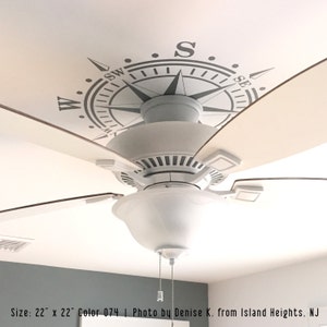 May include: A white ceiling fan with a compass design on the ceiling. The compass is gray and has the letters N, S, E, and W. The fan blades are brown. Size: 22" x 22". Color 074. Photo by Denise K. from Island Heights. NJ