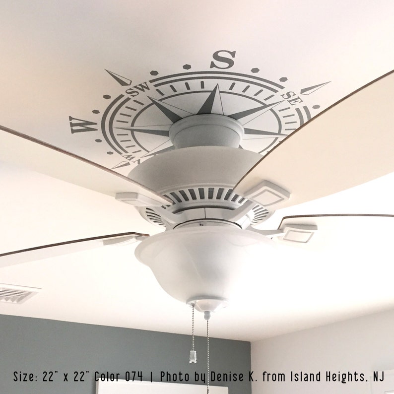 May include: A white ceiling fan with a compass design on the ceiling. The compass is gray and has the letters N, S, E, and W. The fan blades are brown. Size: 22" x 22". Color 074. Photo by Denise K. from Island Heights. NJ