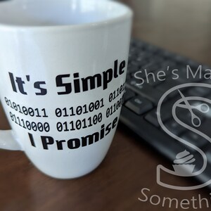 May include: White ceramic mug with black text that reads "It's Simple I Promise" with a series of binary code numbers below the text. The mug is sitting on a wooden surface next to a black keyboard.
