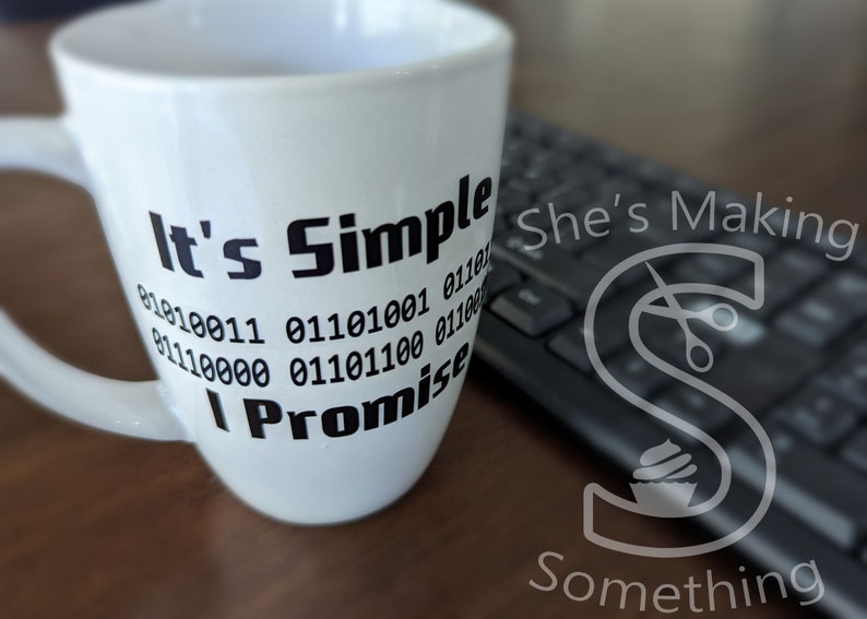 May include: White ceramic mug with black text that reads "It's Simple I Promise" with a series of binary code numbers below the text. The mug is sitting on a wooden surface next to a black keyboard.