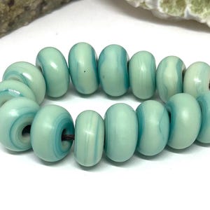 May include: A strand of light green and white glass beads with a swirling pattern. The beads are strung on a brown cord.