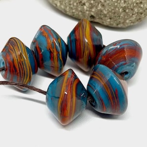 May include: A strand of six colorful glass beads with a swirling pattern of blue, orange, and red. The beads are strung on a brown cord.