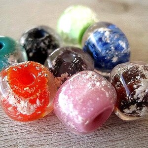 May include: A collection of colorful, translucent glass beads. The beads are in shades of red, pink, blue, green, and brown, with white, cloud-like inclusions. Each bead has a hole for stringing.