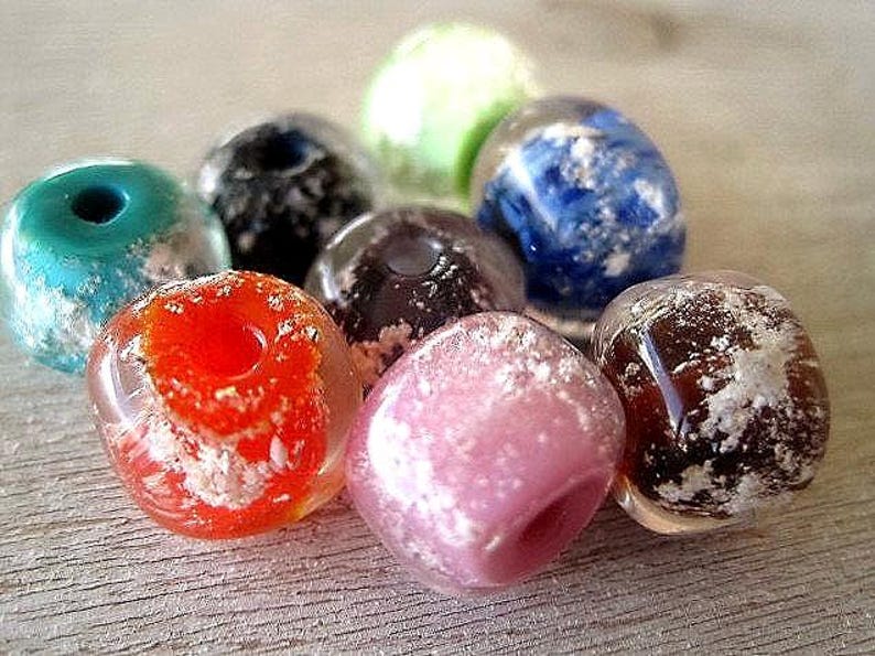 May include: A collection of colorful, translucent glass beads. The beads are in shades of red, pink, blue, green, and brown, with white, cloud-like inclusions. Each bead has a hole for stringing.
