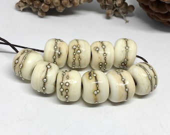 May include: A strand of white bone beads with silver accents. The beads are round and have a smooth, polished finish. The silver accents are in the form of dots and lines.