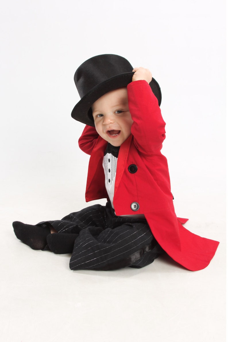 May include: A baby wearing a red tuxedo jacket with a black top hat and black and white striped pants.
