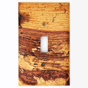 May include: A wooden light switch cover with a natural wood grain pattern. The cover has a rectangular opening for the switch and two small holes for screws. The wood features shades of brown, tan, and black.