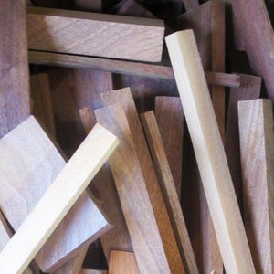 Könnte beinhalten: Eine Ansammlung verschiedener Holzbretter und -blöcke in Braun- und Beigetönen. Die Stücke variieren in Größe und Form, einige sind rechteckig, andere quadratisch. Die Holzmaserung ist sichtbar, was auf ein natürliches Material hindeutet.