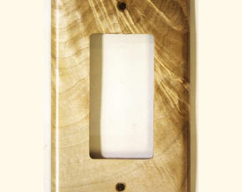 May include: A rectangular light brown wooden light switch cover plate featuring a prominent natural wood grain pattern. The plate has a central vertical rectangular cutout and two small circular screw holes positioned at the top and bottom.