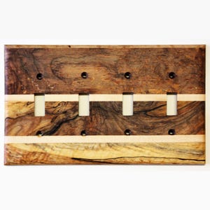 Könnte beinhalten: Eine Holz-Lichtschalterplatte mit einem dunklen braunen und hellen Holzmaserungsmuster. Die Platte hat fünf Öffnungen für Lichtschalter und ist aus zwei verschiedenen Holzarten gefertigt.